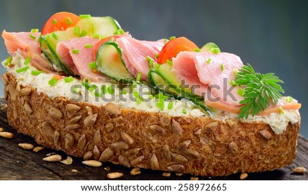 Summer ham salad sandwich. Open sandwich of ham, cucumber and tomato on a slice of whole grain bread with cream cheese and chives garnish.