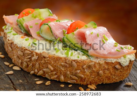Ham sandwich. Open sandwich of ham, cucumber and tomato on a slice of whole grain bread with cream cheese and chives garnish.