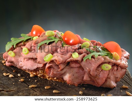 Beef and salad open sandwich. Roast beef, thinly sliced with ruccola, spring onion and tomato garnish on a slice of whole grain bread.