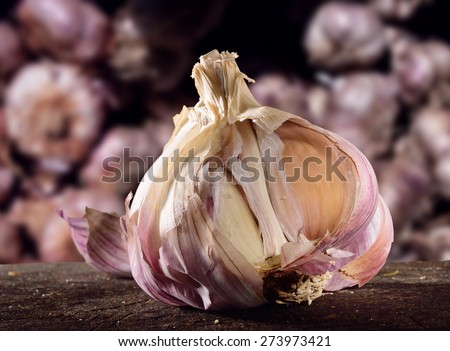 Garlic on rustic wooden surface with stacked purple garlic bulbs as background. Selective focus close up on bulb.