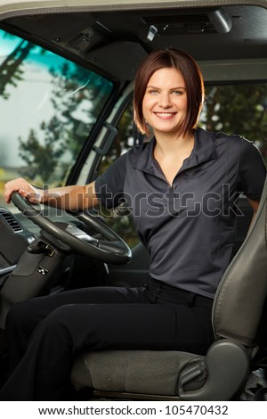 A woman in work uniform sits in the driver\'s seat of a delivery truck, smiling at camera.