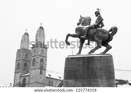 snow covered statue of rider on a horse by the limmat river, a seagull stands on his head, the towers of grossmunster church on the back ground (black and wight)