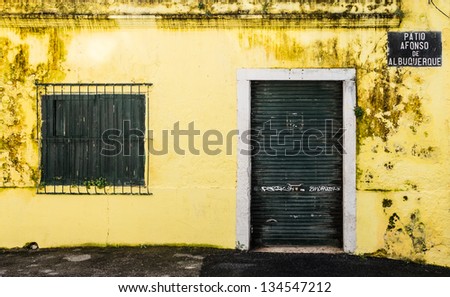 Facade of the front of an abandoned building with green door and window, yellow wall