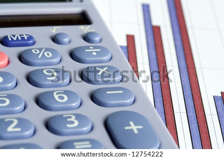 Close up of a blue calculator next to a red and blue bar chart on a white background