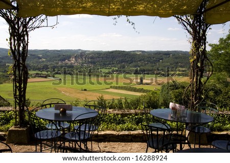 View of Beynac Castle in the Dordogne valley, France, with cafe tables and chairs set out on the terrace in the foreground