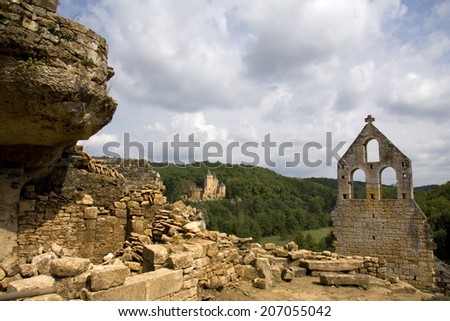 View of a French castle across the valley with a ruined church and rocks in the foreground