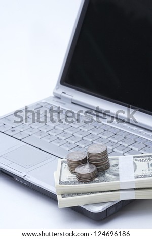 Laptop with stacked coins and bundles of bills, close up