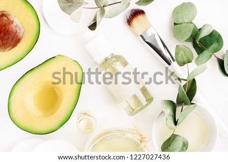Avocado oil natural skin care & hair treatment. Green organic ingredients & essential oil cosmetic bottle, top view white table.