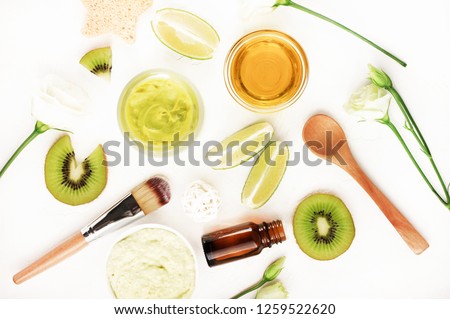 Top view nourishing natural skincare. Body balm & lime kiwi fruit slices, essential oils and face mask, bowl of honey, roses. Green ingredients white table background flat lay.