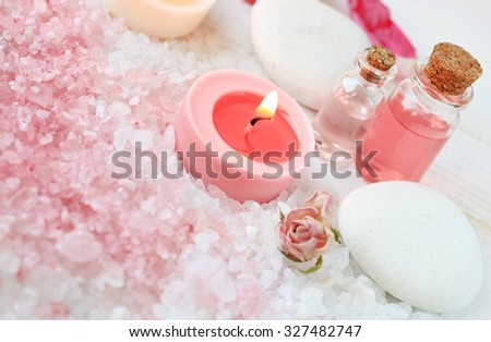 Tranquil spa relaxation setting pink white bath salt, candles, aroma essence bottles, spa stones. Soft focus