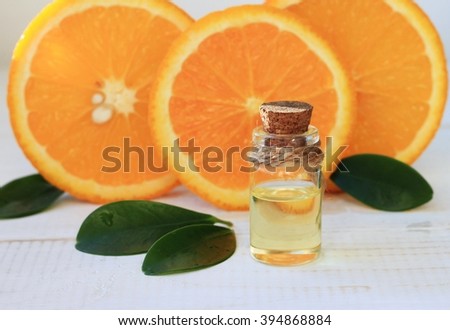 Essential orange oil in bottle, fresh fruit slices on background. Natural fragrances.