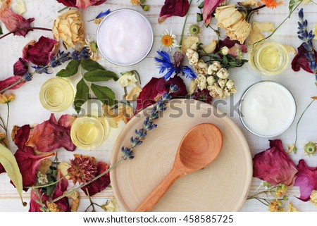 Dried herb mix, wooden plate spoon, moisturizer, lotion, essential oils. Herbal skincare spa preparation, top view.