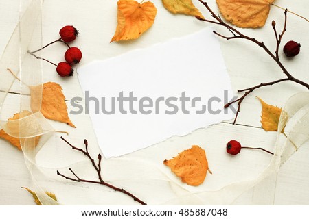 Blank white paper note framed dried yellow autumnal leaves, bare branches, red berries. Fall background.