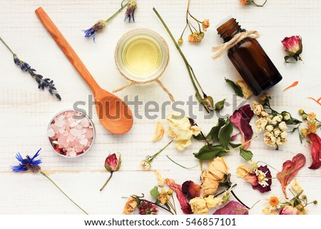 Herbal cosmetic ingredients top view wooden background. Mix of dried holistic flowers scattered, salt, massage herb-infused oil, aroma dropper bottle, spoon