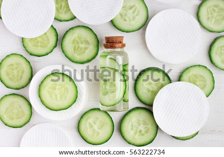Fresh homemade refreshing facial toner in bottle, green cucumber slices, cotton-pads, top view ingredients