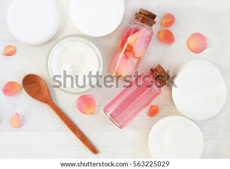 Handmade rose extract cosmetic. Tonic and cream, cotton pads, bottles, fresh pink flower petals, wooden table preparation background.