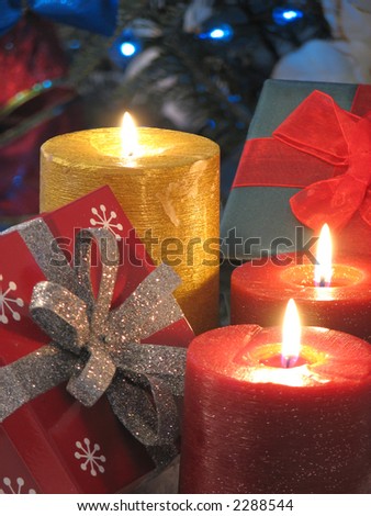 Shot of three burning candles and a couple gifts. Christmas tree with blue lights used as a background.  LOW LIGHT.