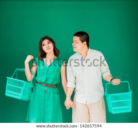 asian couple holding empty supermarket cart in green background