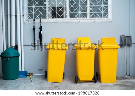 yellow plastic trash bin against building wall with cleaning equipment- bloom and mob