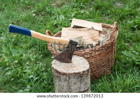An axe stuck in a log in front of basket with logs fire