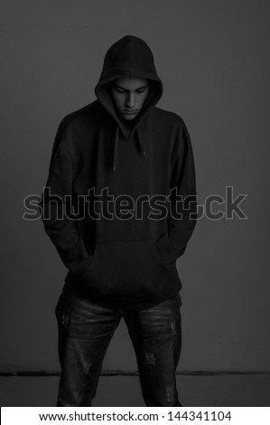 Black and white photo of teenager with hoodie looking down against a dirty gray wall