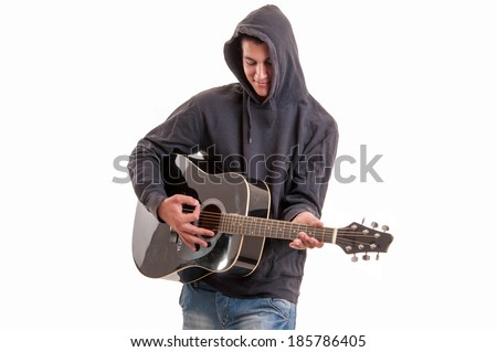Young man dressed  in hoodie try to understand how to play acoustic guitar, studio shoot. pleased to play an instrument