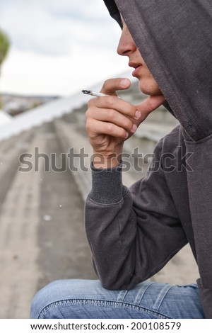 Young man in depression smoking a cigarette on a stadium. Concept of young people with harmful habits