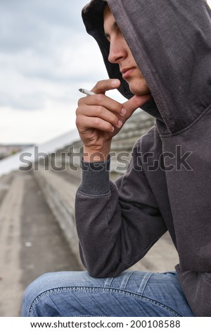 Young man in depression smoking a cigarette on a stadium. Concept of young people with harmful habits