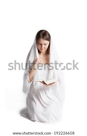 Young woman with a veil kneeling and reading the Bible. Isolated on a white background