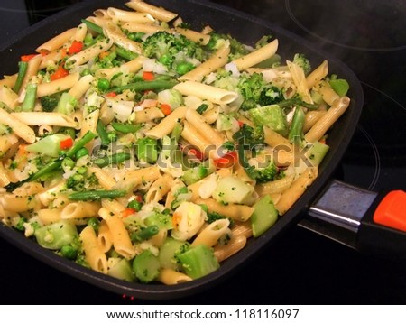 Cooking mixed vegetables with pasta. Fried mixed vegetables with pasta  in the black pan. Close-up.