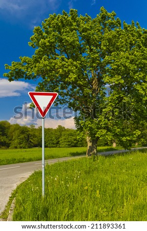 Give away traffic sign near trees and road