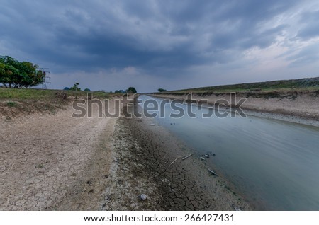 View of river, cloud and Cracked soil upon cloudy sunset.There are bunch of cloud dried river and cracked soil. There is one small tree in the scene.