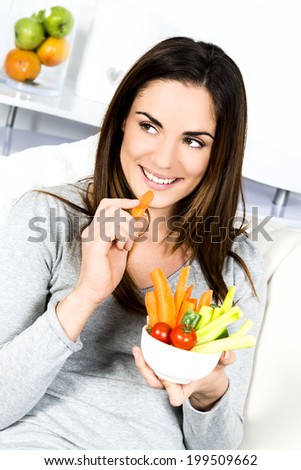 Woman eating salad. Beautiful healthy smiling Caucasian woman enjoying a fresh healthy salad sitting in sofa looking up. High angle view with copy space on modern interior.