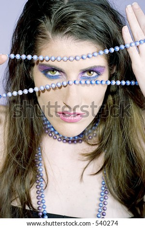 Attractive young woman gazing through painted pearls and wearing matching eye makeup