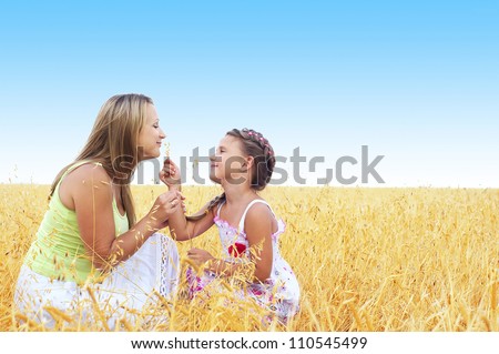 Young mother and her daughter at the wheat field on a sunny day