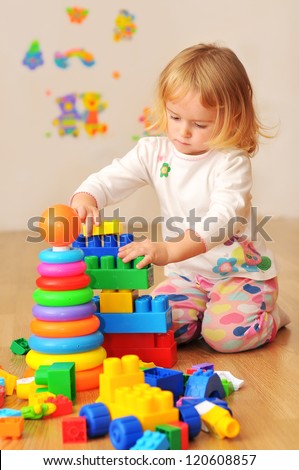 Kid playing with wooden blocks laying on the floor in their room