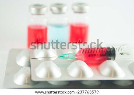 Red liquid in disposable syringe on blister pack on medicine vials background