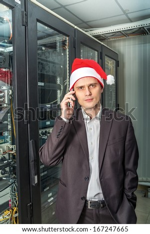 network engineer in server in a cap of Santa Claus with mobile phone