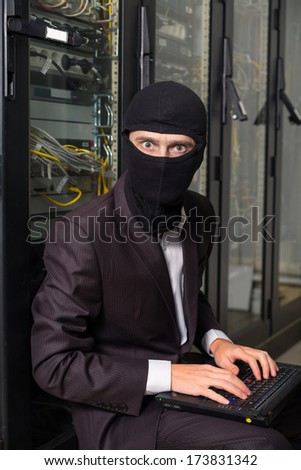 robber in black mask in the server room hack, and steals information, unauthorized downloading data on a laptop