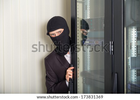 robber in black mask hack server room unauthorized downloading data on laptop