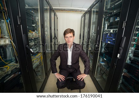 Network Engineer in the server room in a suit sitting on a chair, distorted perspective