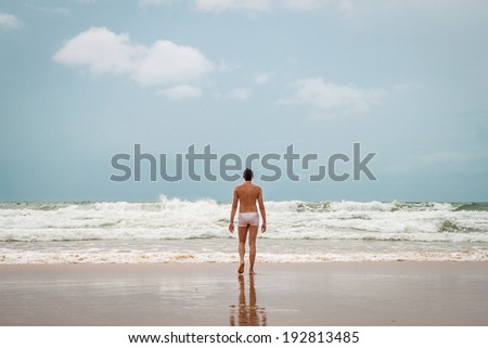young man goes to sea water, the view from the beach, clouds on the horizon, back
