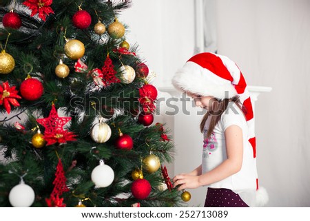 little girl in a red cap hangs on the Christmas tree new year toys