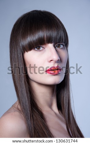 Beauty studio portrait of pretty young woman model with straight hair, long straight fringe, natural makeup, bright colorful red glossy lips half open, looking at camera. Gray background, copy space