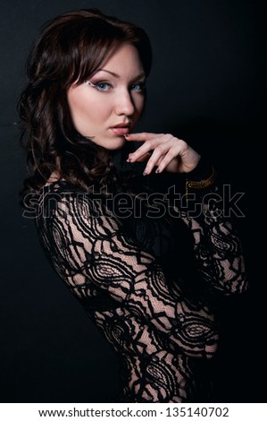 Mysterious beautiful young adult sexy woman model with long hair in locks and curls wearing black transparent lace top, holding her hand near lips, looking at camera. Black background
