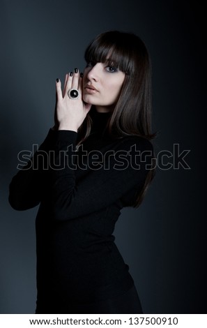 Studio portrait of beautiful woman model with straight long hair, wearing black clothes, black manicure, jewelry ring with black stone in the center and small diamonds around. Gray background