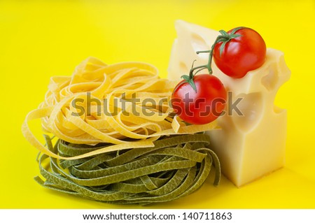 Tasty colorful bright still life of traditional Italian green and yellow pasta nests, cheese with holes, two ripe fresh shiny red cherry tomatoes with green stems on top. Yellow background, copy space