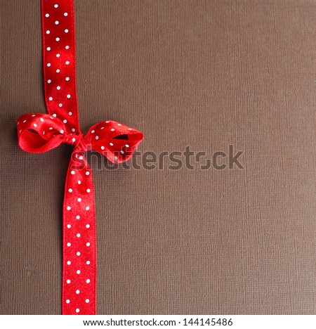 Red dotted satin ribbon and bow against brown paper background with slight pattern. Copy space