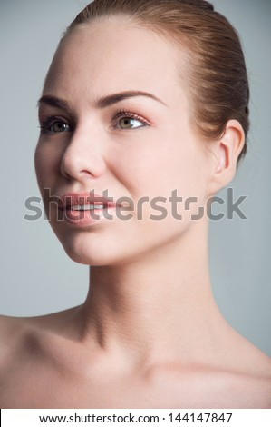 Closeup portrait of beautiful young woman model with clear facial skin, tender natural makeup, hair pulled back, looking aside. Gray background