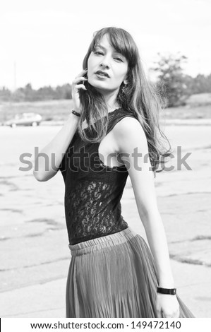 Black and white portrait of young pretty brunette woman model wearing pleated skirt and lace top, walking outdoors and looking at camera over her shoulder
